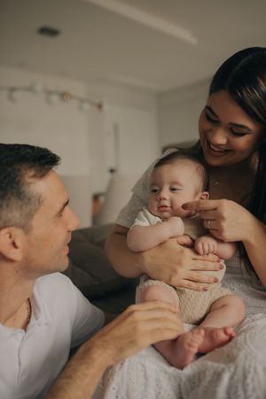 Intimate family moment as parents bond with their smiling baby on a bed.