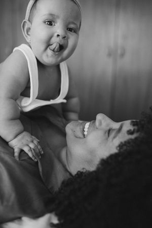 Black and white portrait of a playful baby sticking out tongue while laying on adult.