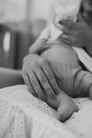 Black and white close-up of gentle hand holding baby's foot on textured fabric.