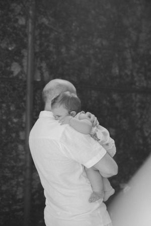 Black and white photo of tender embrace between adult and baby outdoors.