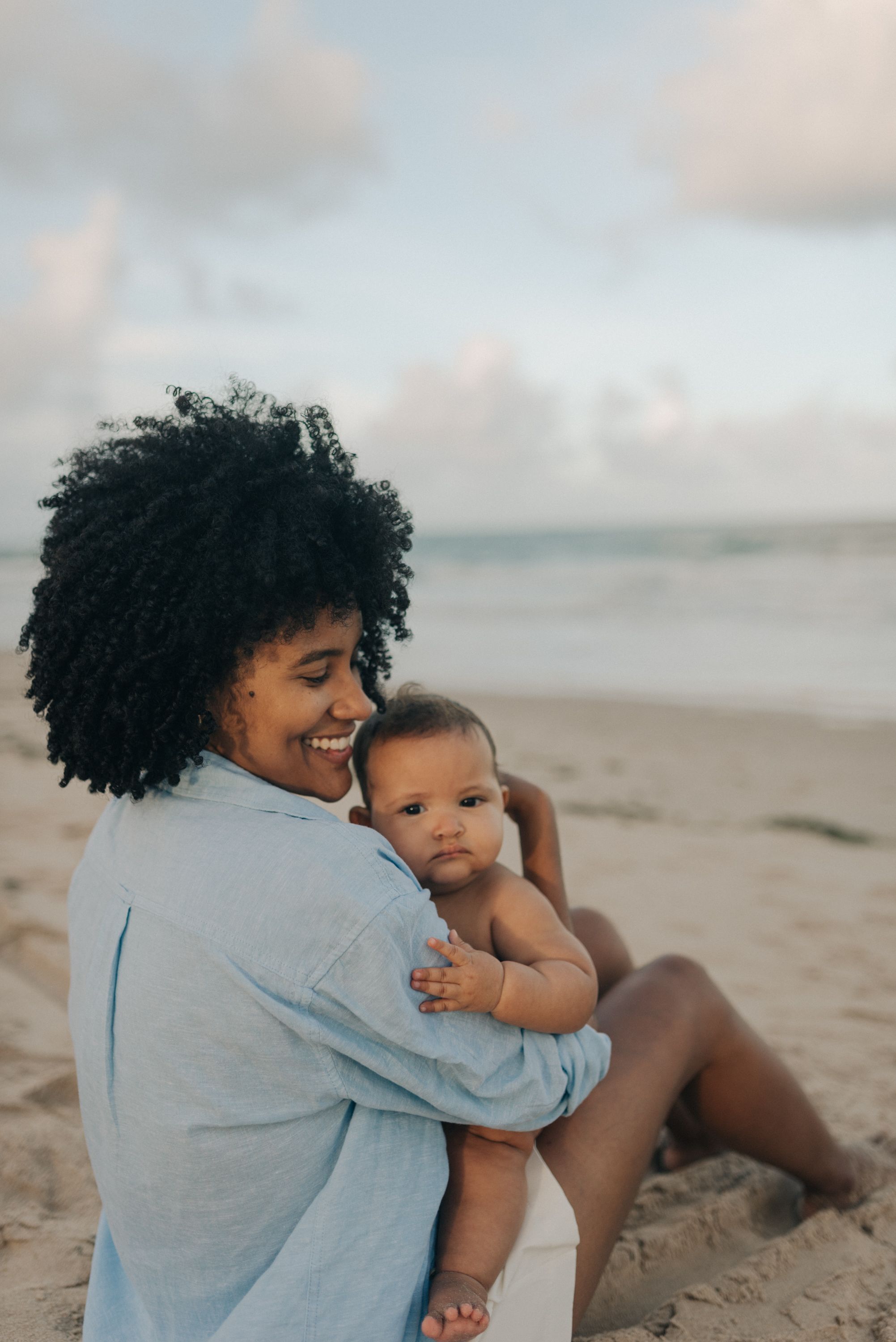 Parent and baby sharing a joyful moment while sitting on sandy beach at sunset.