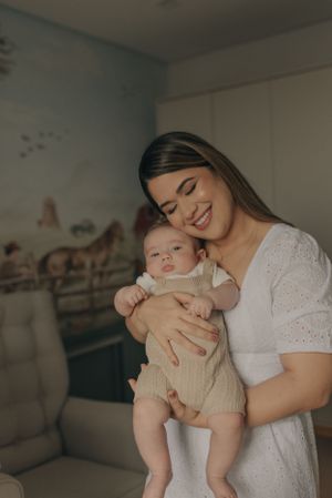 Joyful indoor portrait with baby in beige outfit against nursery wall decor.