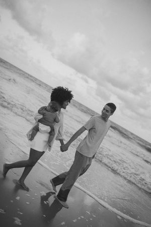 A couple holding hands and walking together on a beach in black and white.