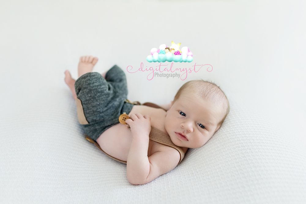 Infant wearing navy blue bottoms lying on soft white textured surface.