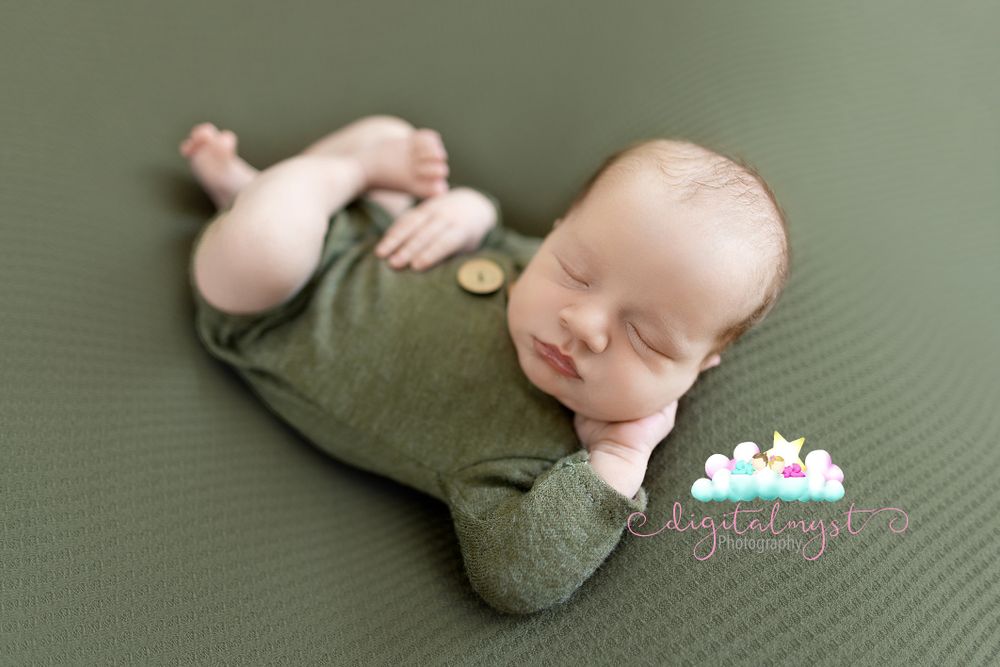 Sleeping newborn in green outfit during professional photo session.