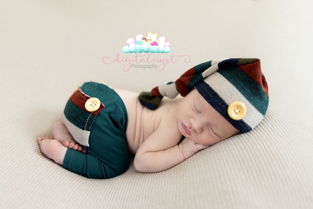 Newborn baby sleeping peacefully in navy blue outfit against light background.