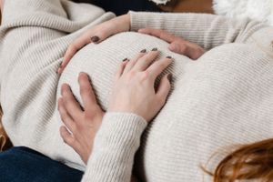 Hands gently resting on a growing belly in a warm indoor setting.
