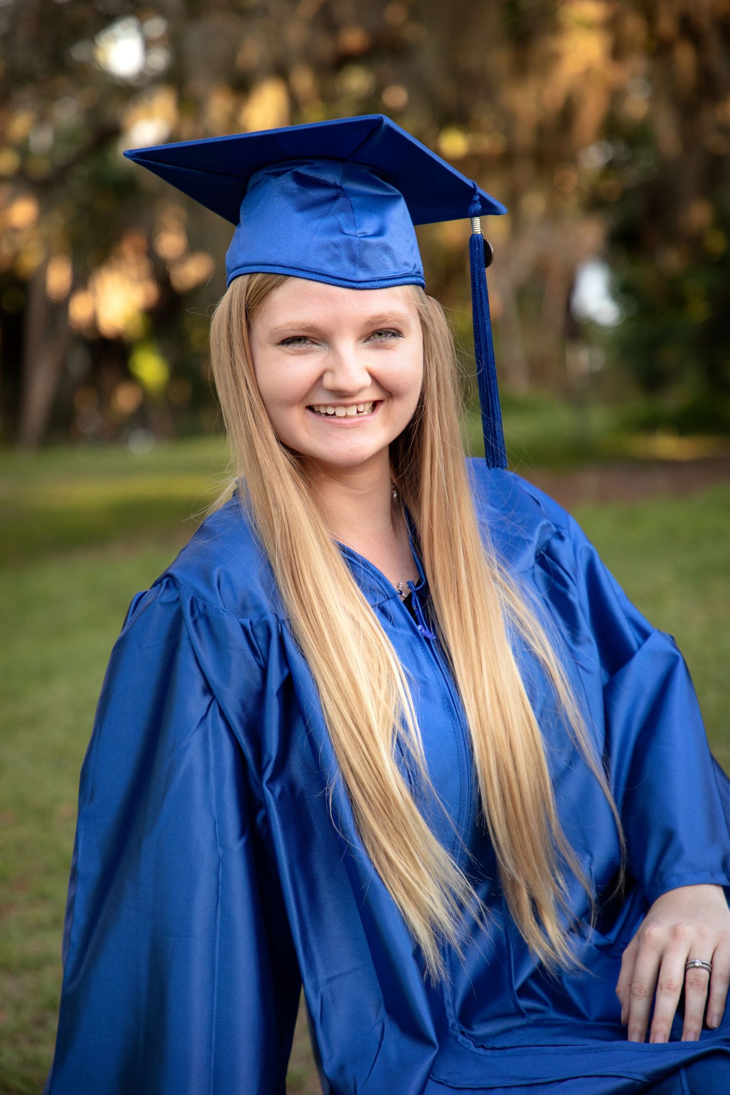 Recent graduating girl with long blonde hair in blue cap and gown.