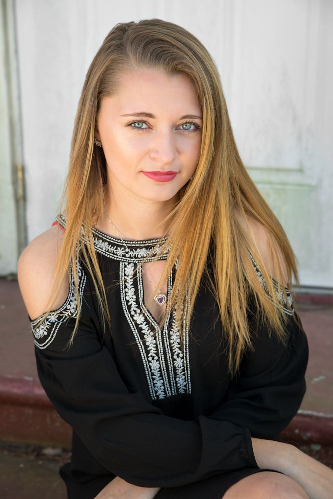 Girl in black dress sitting on step in front of a white door.