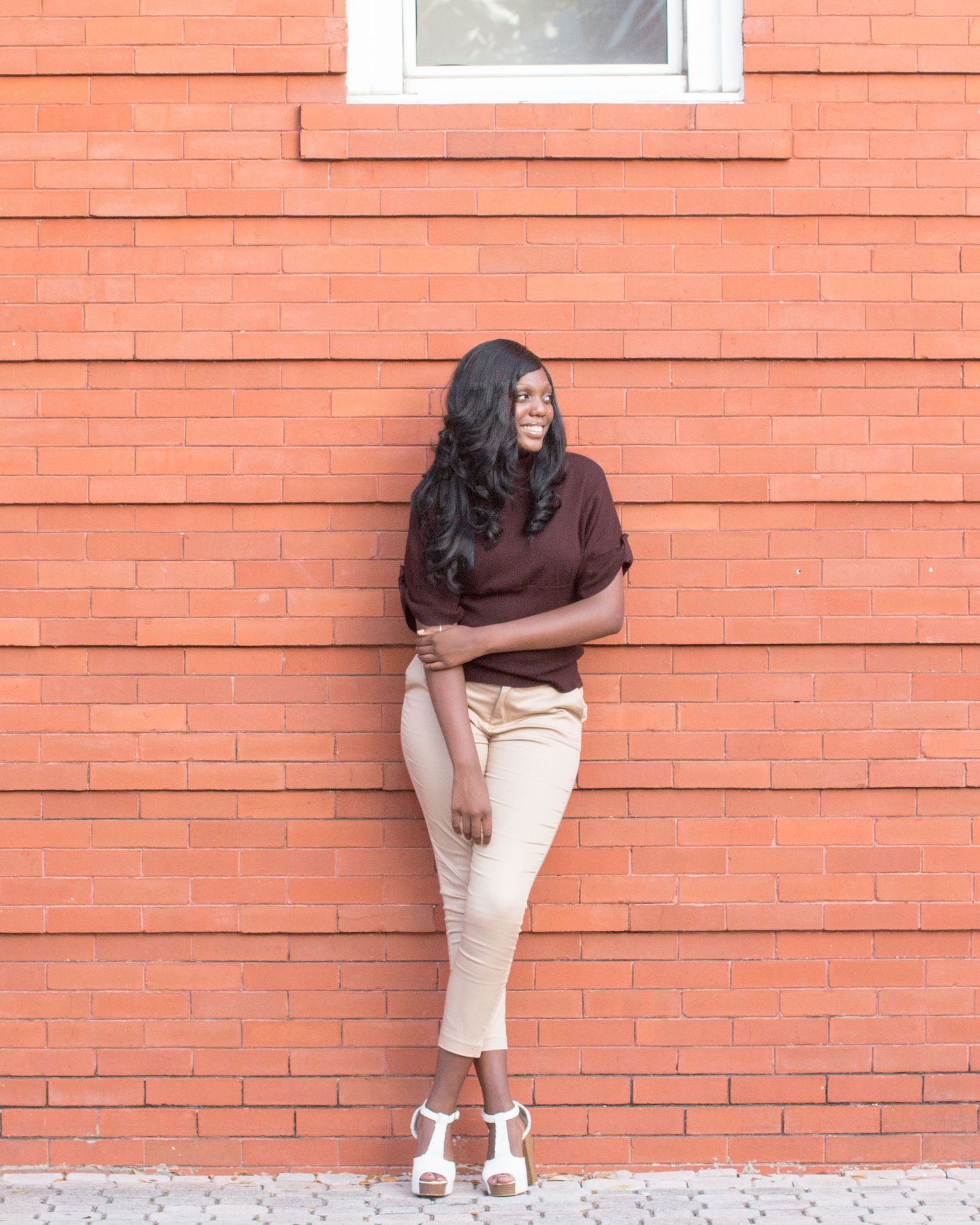 Tall young lady in brown shirt and tan pants leaning against a brick wall in Dunedin Florida.