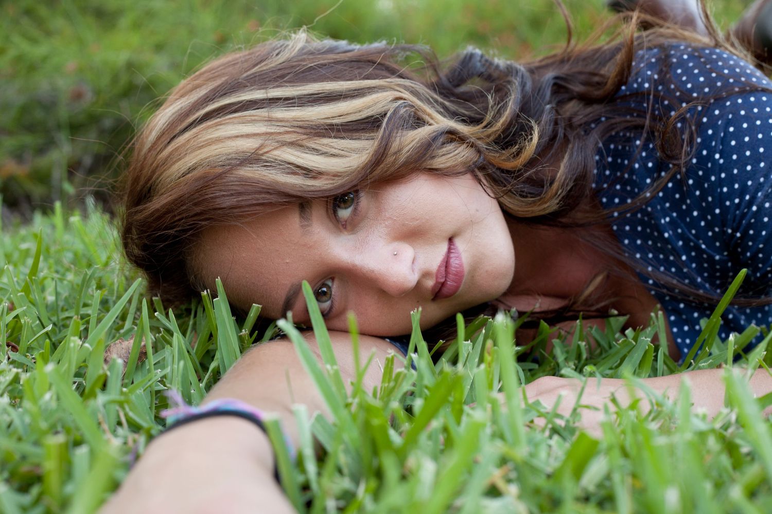 Girl in blue and white polka dot dress laying in the grass.