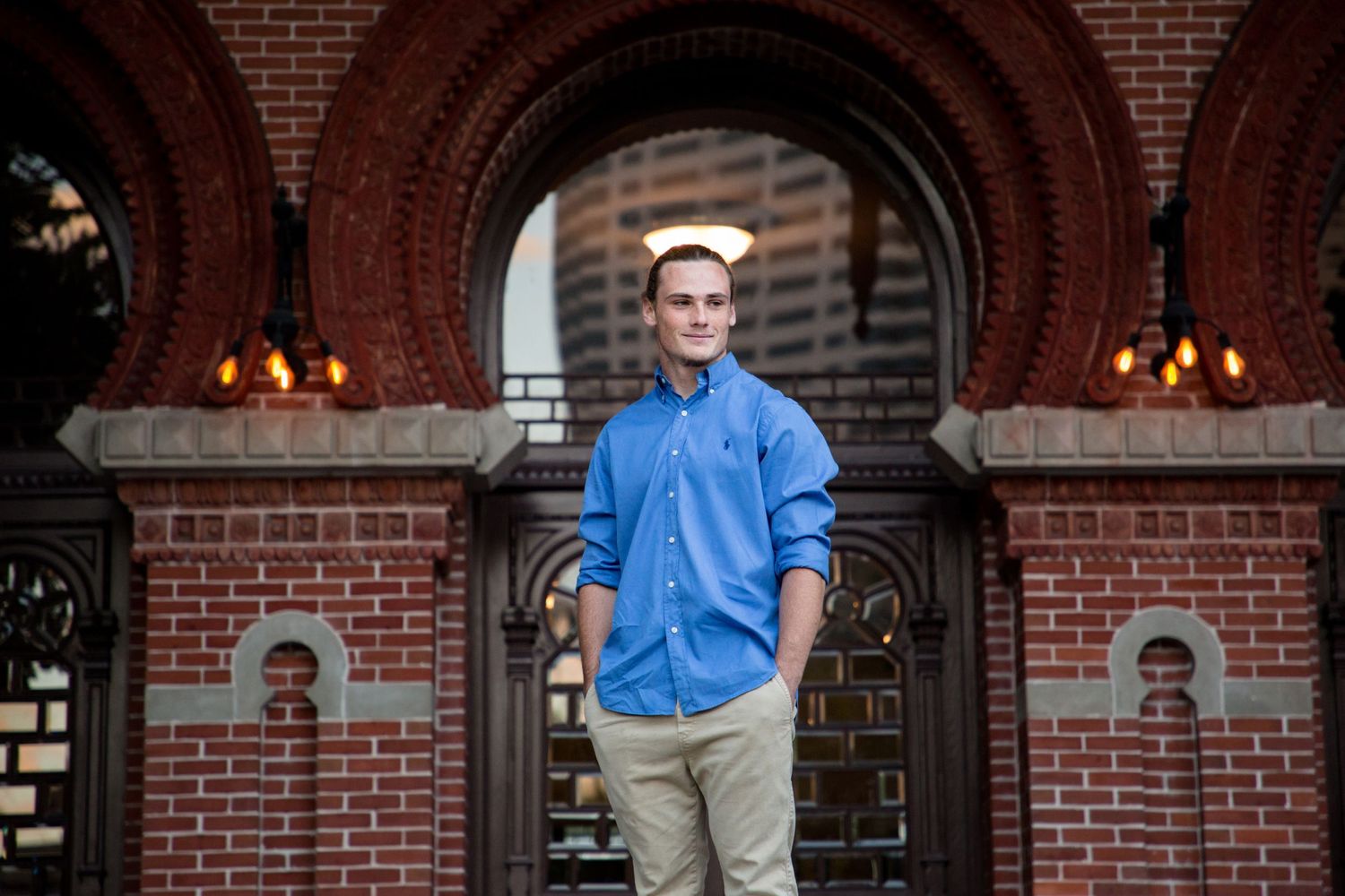 Young man in blue shirt and tan pants standing outside the doors to the University of Tampa.