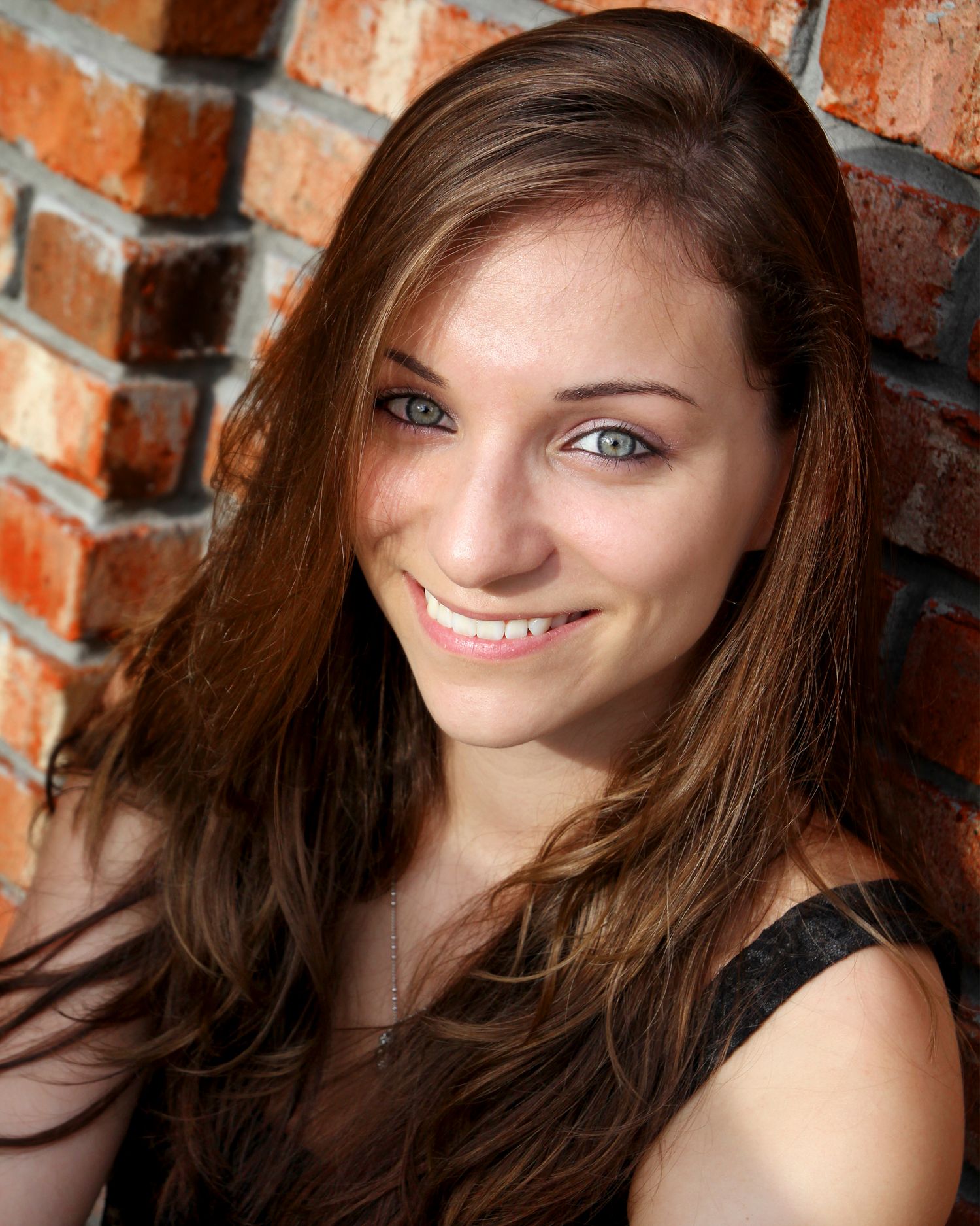 Teenage girl with black shirt and brown hair sitting against a red brick wall.