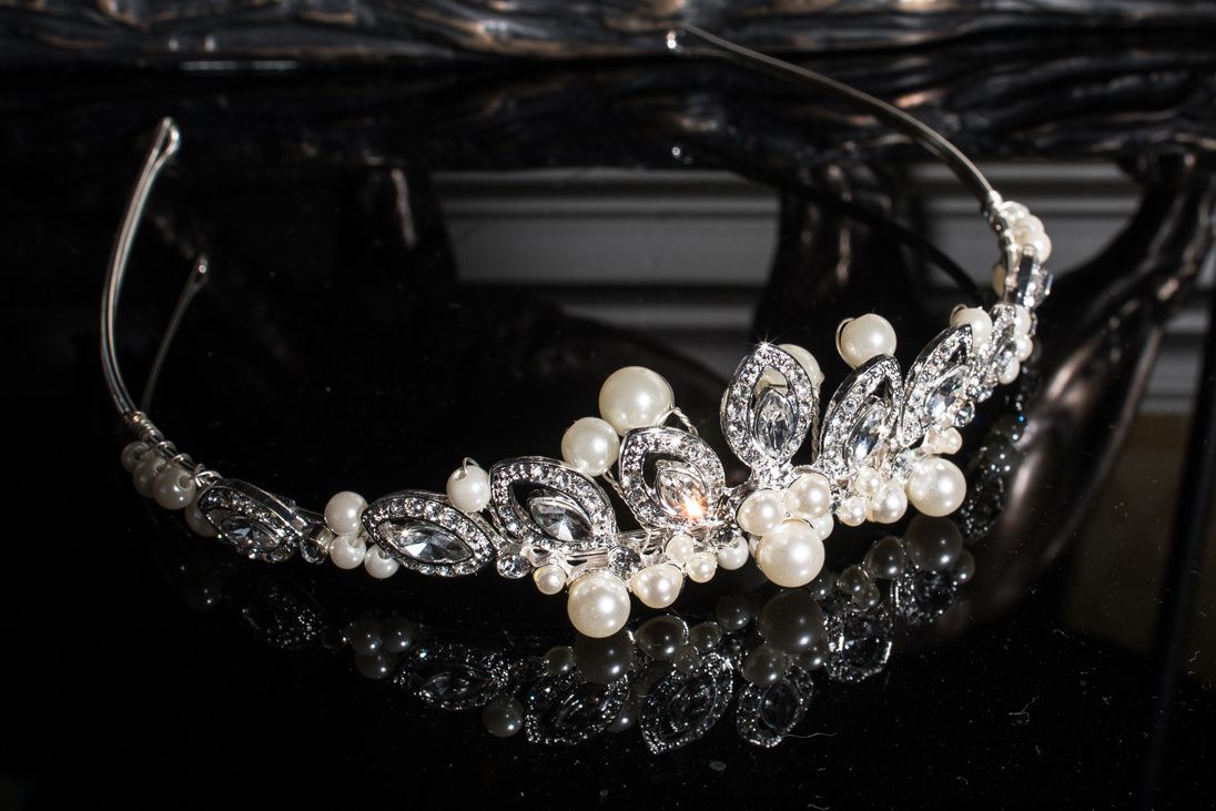 Crystal and pearl bridal tiara displayed on reflective black surface.