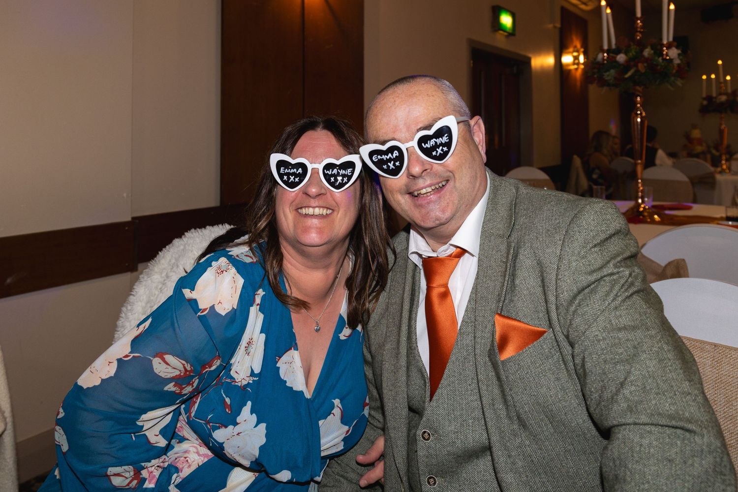 Event guests in formal attire wearing matching heart glasses while enjoying celebration.
