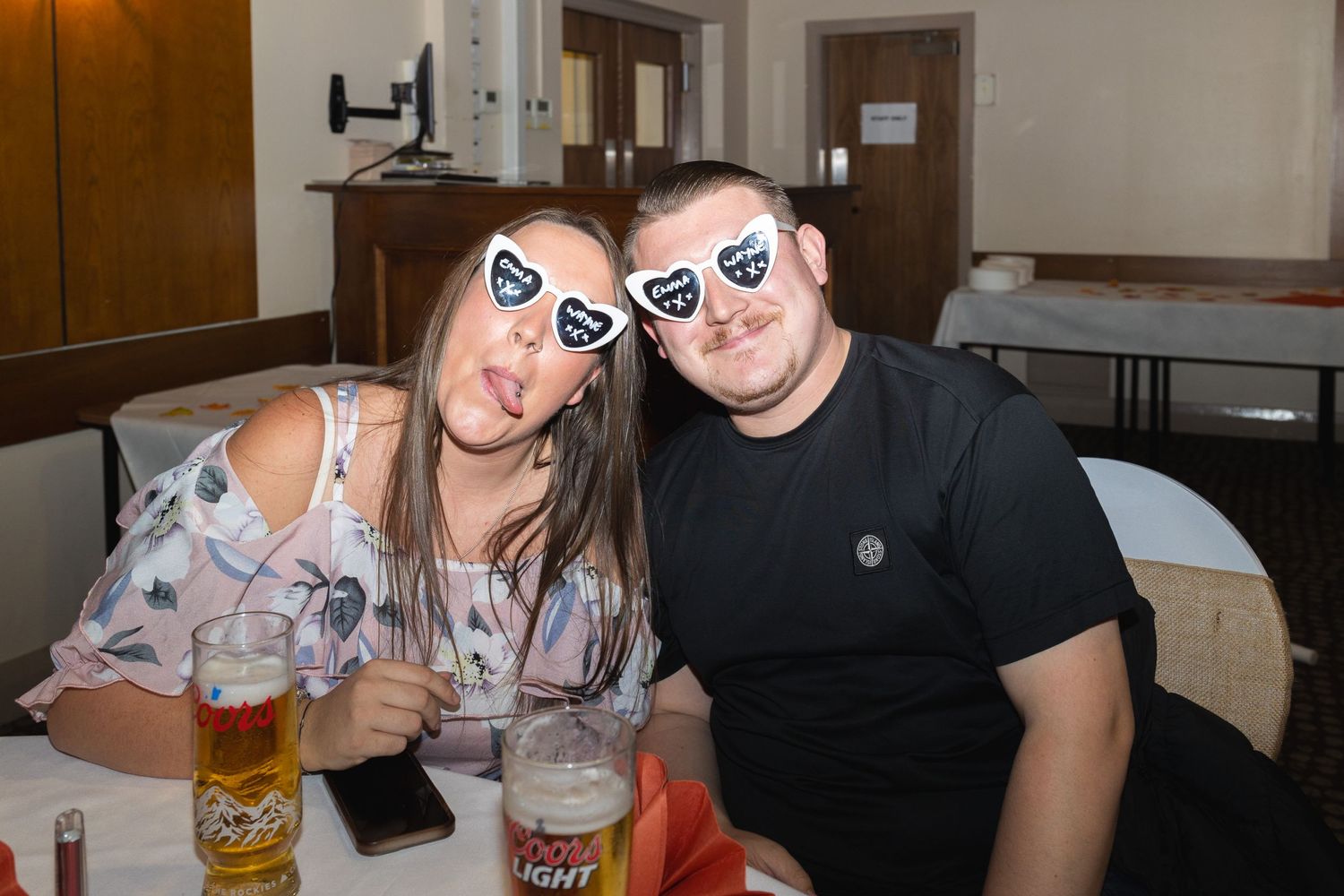 Two guests at an event wearing matching novelty glasses while enjoying drinks.