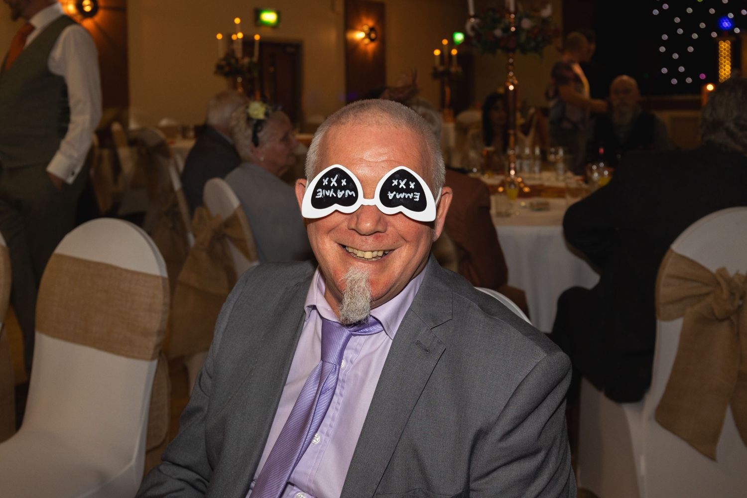Guest enjoying a formal event wearing festive heart-shaped glasses in a reception hall.