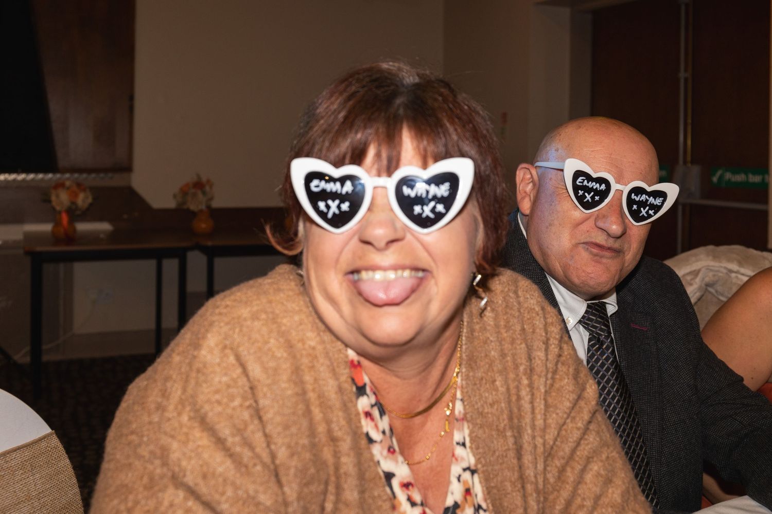 People wearing heart-shaped novelty sunglasses smiling at a social event.