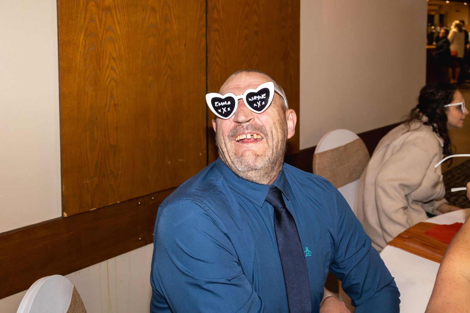 Person wearing heart-shaped novelty sunglasses and a blue dress shirt at an indoor event.