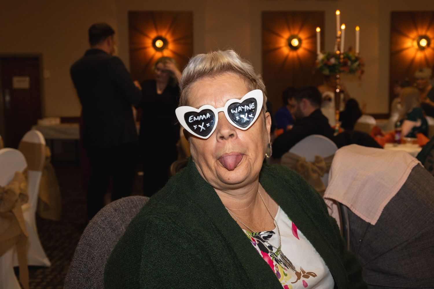 Party guest in dark jacket wearing decorative heart-shaped glasses at a formal event.