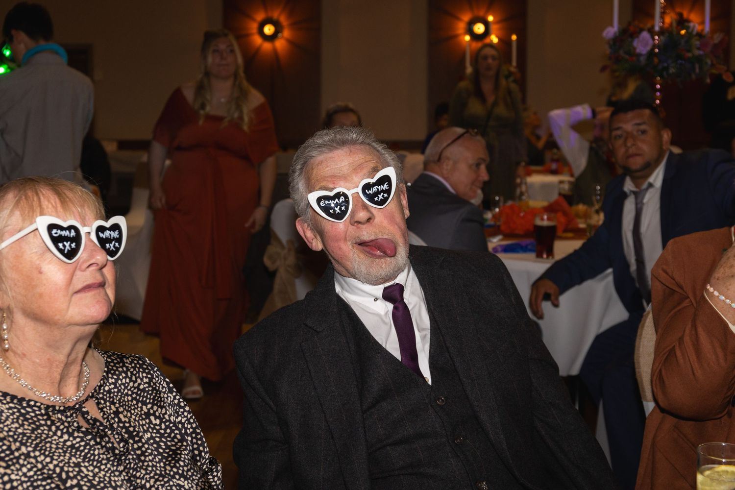 Two guests in formal attire wearing matching heart-shaped sunglasses at evening event.