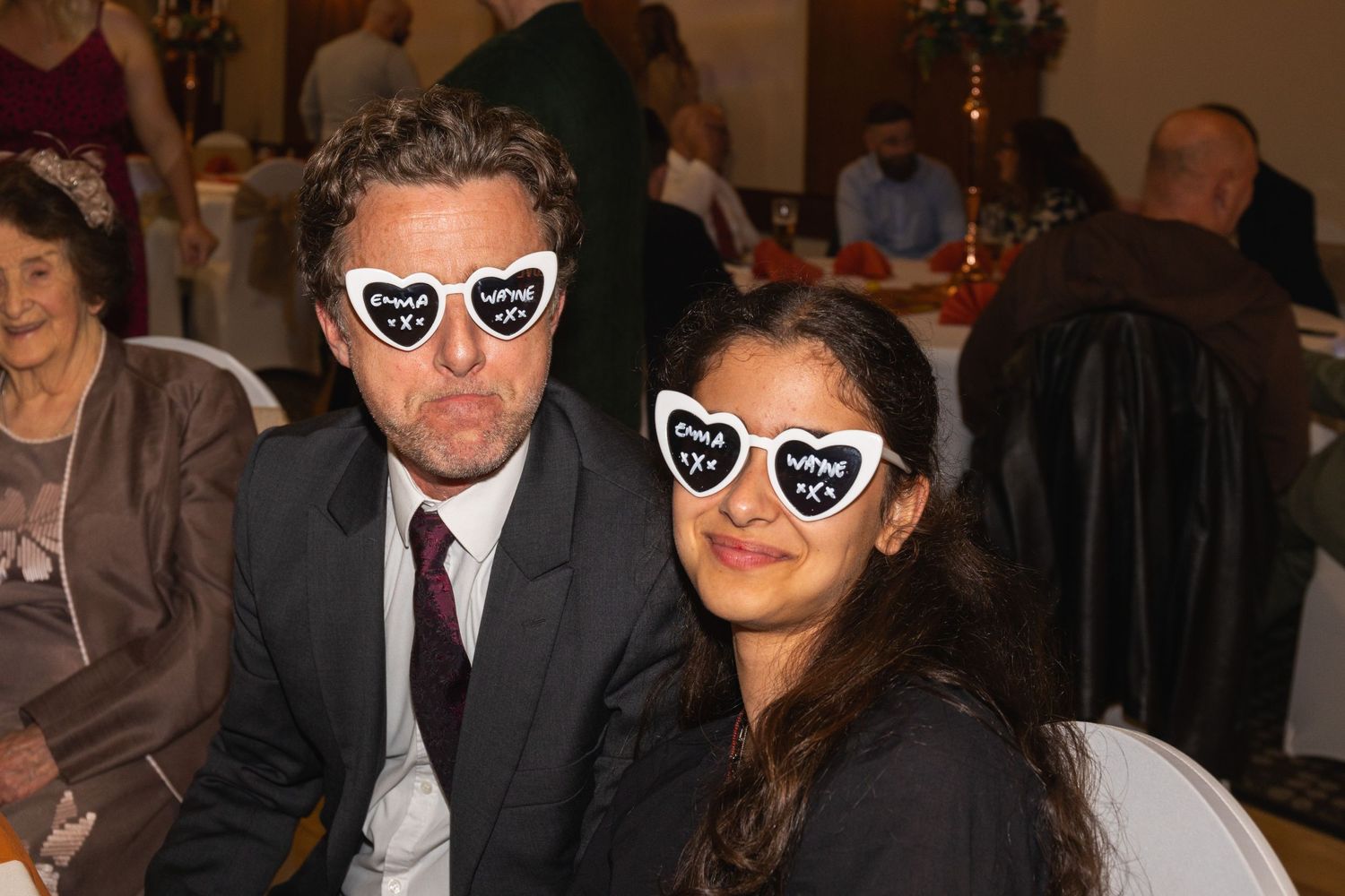 Couple in formal attire wearing matching heart-shaped sunglasses at evening event.