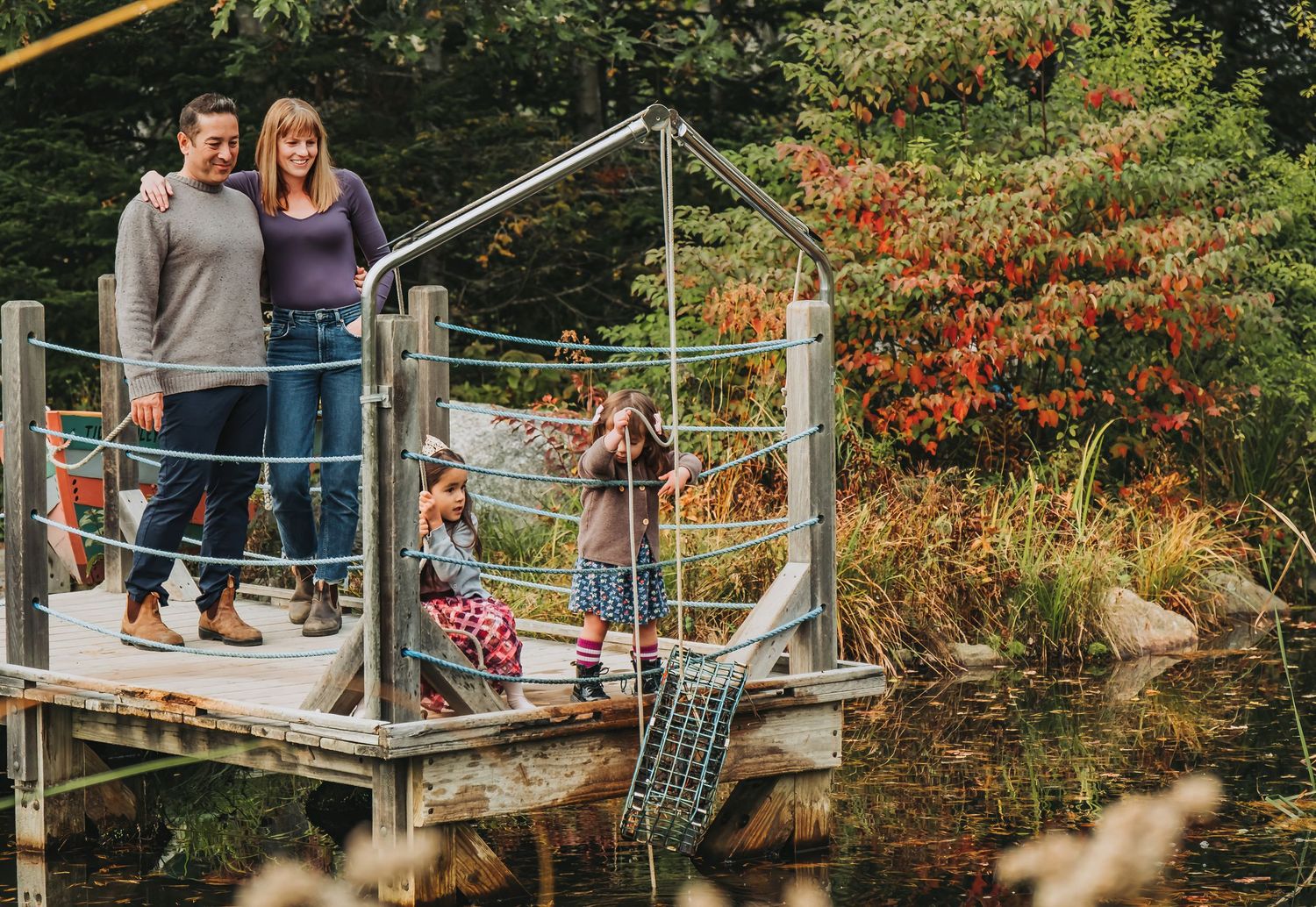 A Mom and Dad look on as their adorable daughters play near the water at the Maine Botanical Gardens.