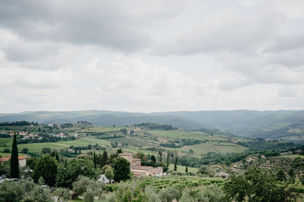 Panoramic view of rolling green hills and countryside in Tuscany with cypress trees and distant mountains.