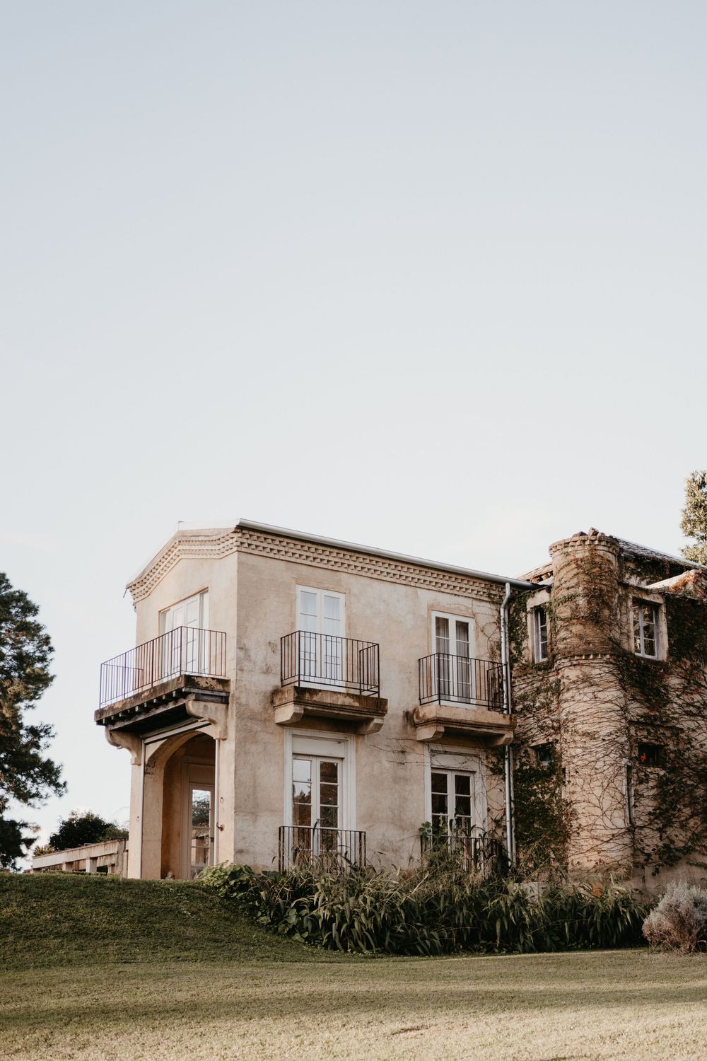 Mediterranean-style villa with stone facade and balconies sits on grassy hillside.