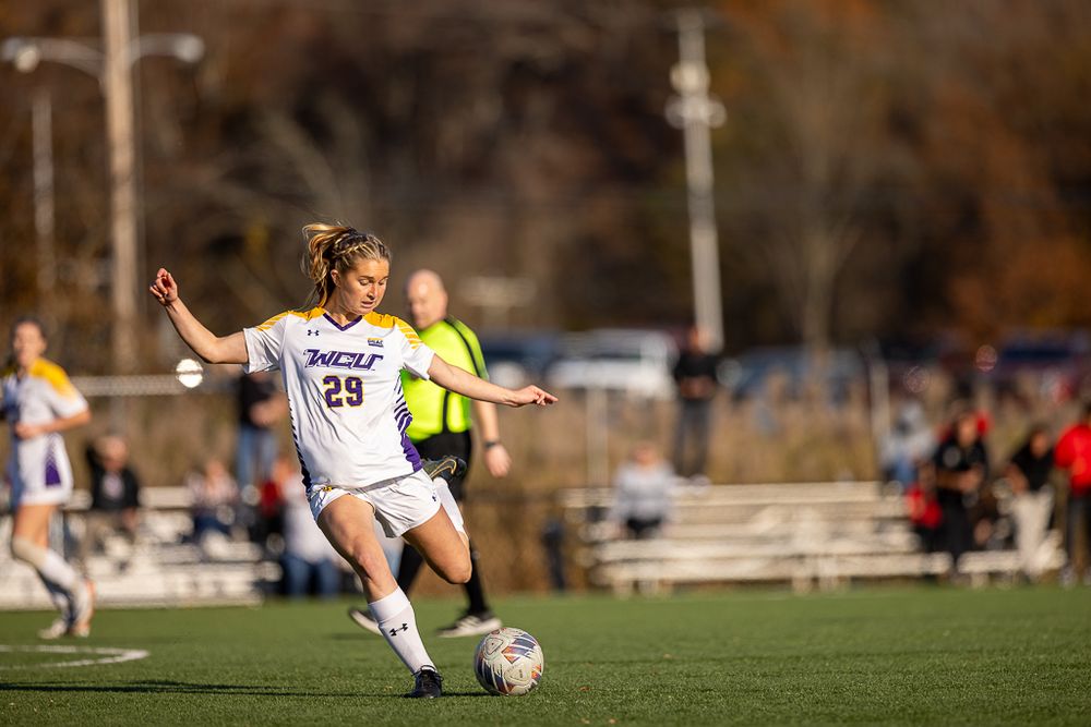 Soccer player in white uniform strikes ball during competitive match on sunny field.