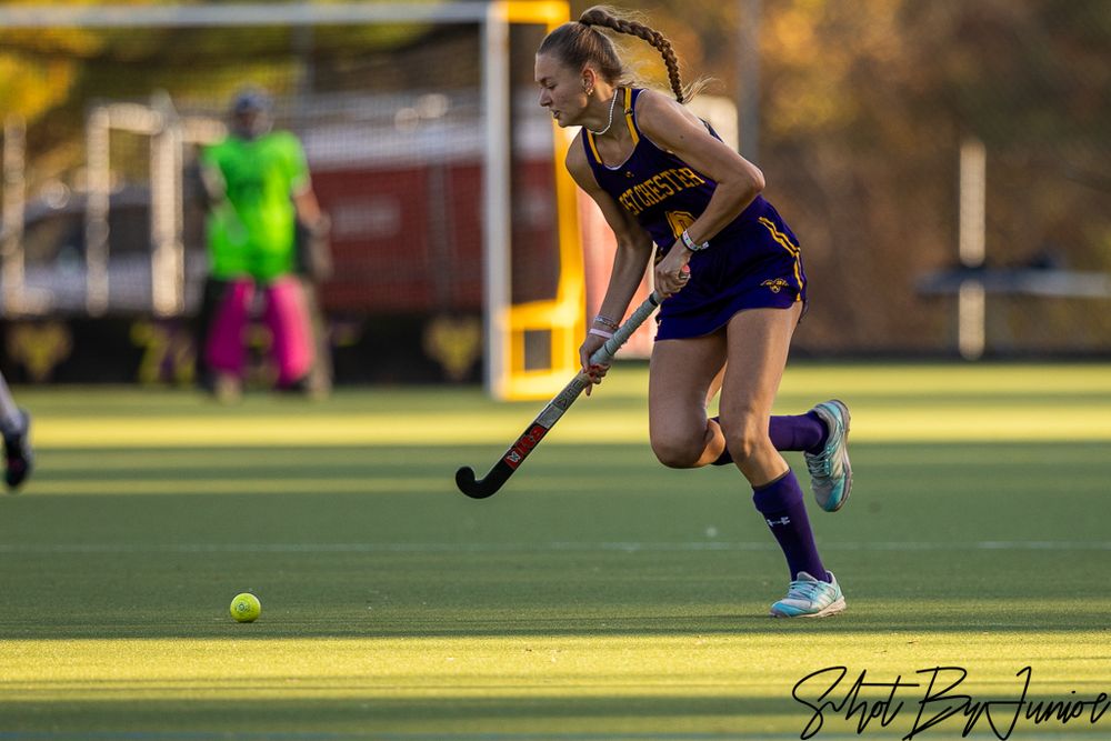 Field hockey athletes duel for ball control during an intense match at sunset.