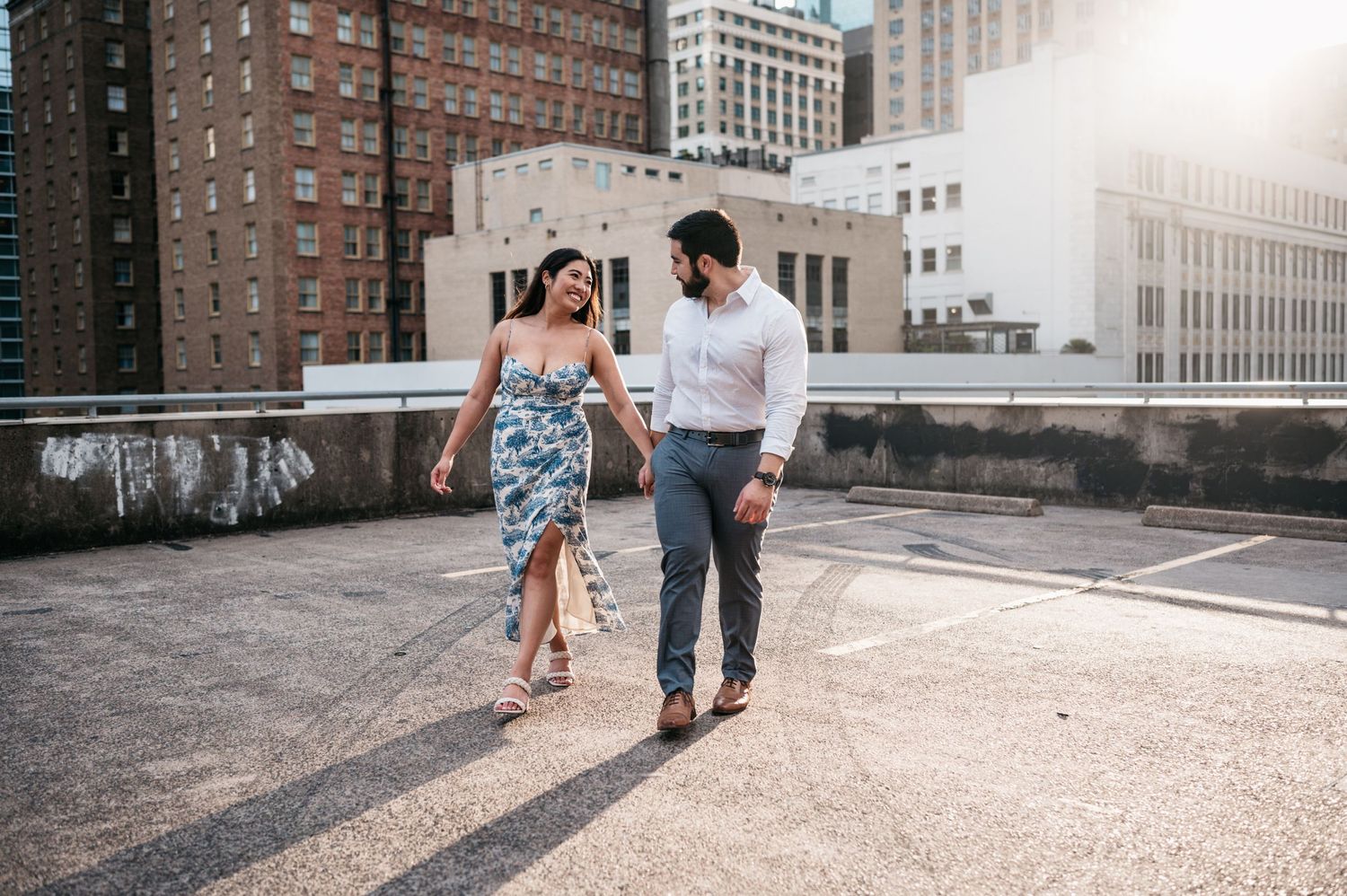 A couple walks together on a rooftop with city buildings in the background.