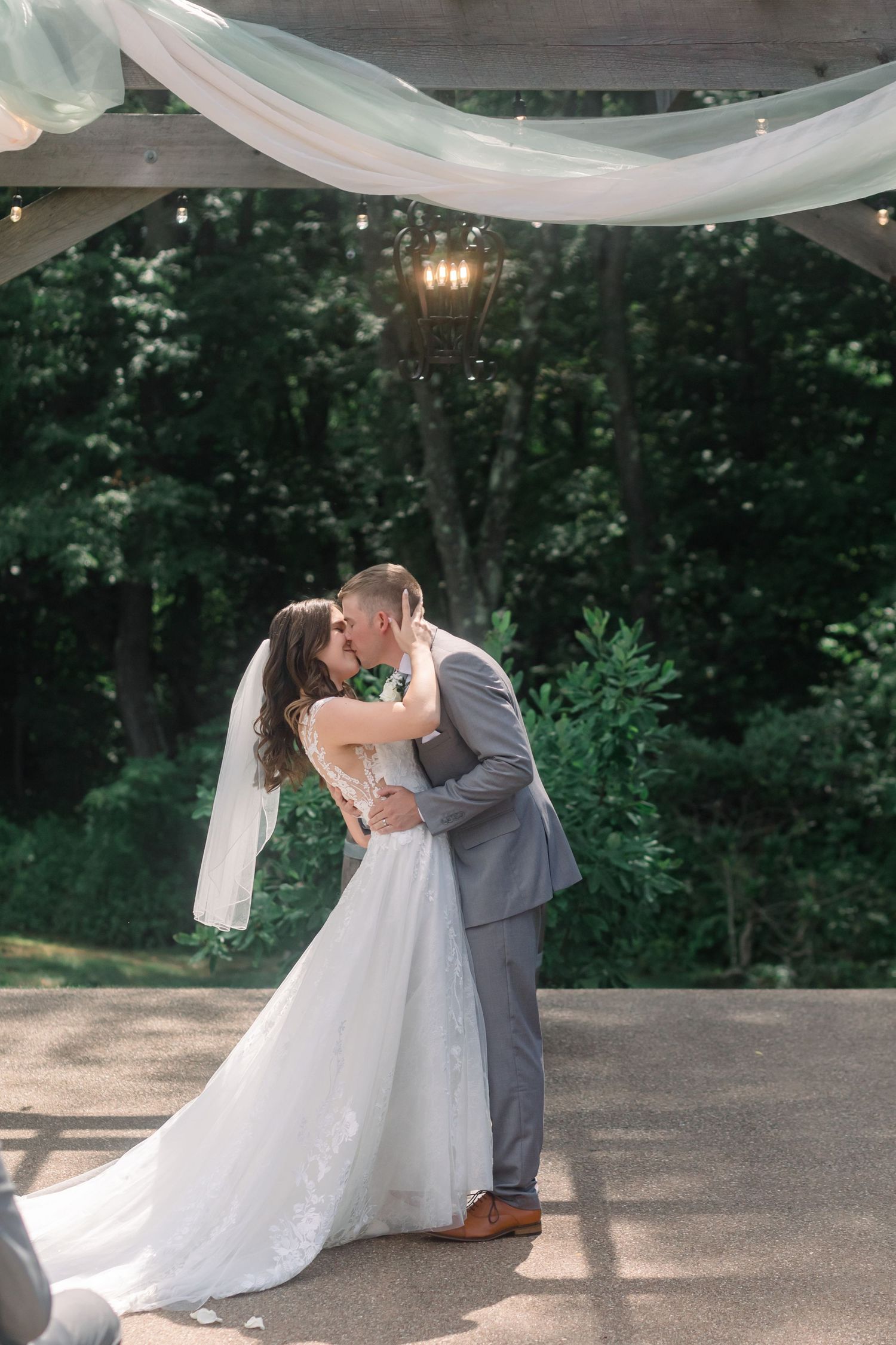 Newlyweds share romantic dance under white fabric draping and string lights at outdoor reception.