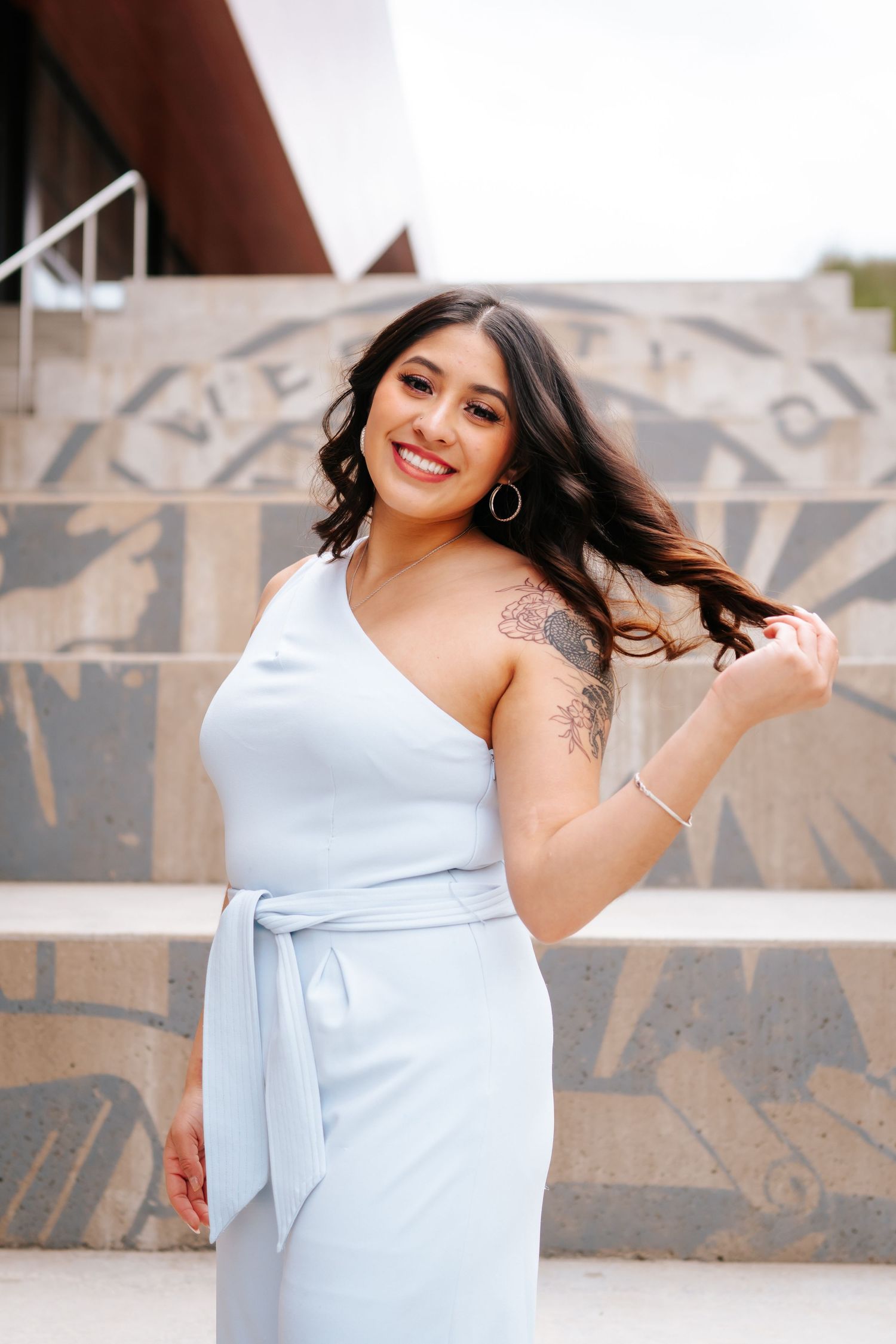 Woman in a light blue formal dress poses on concrete steps.