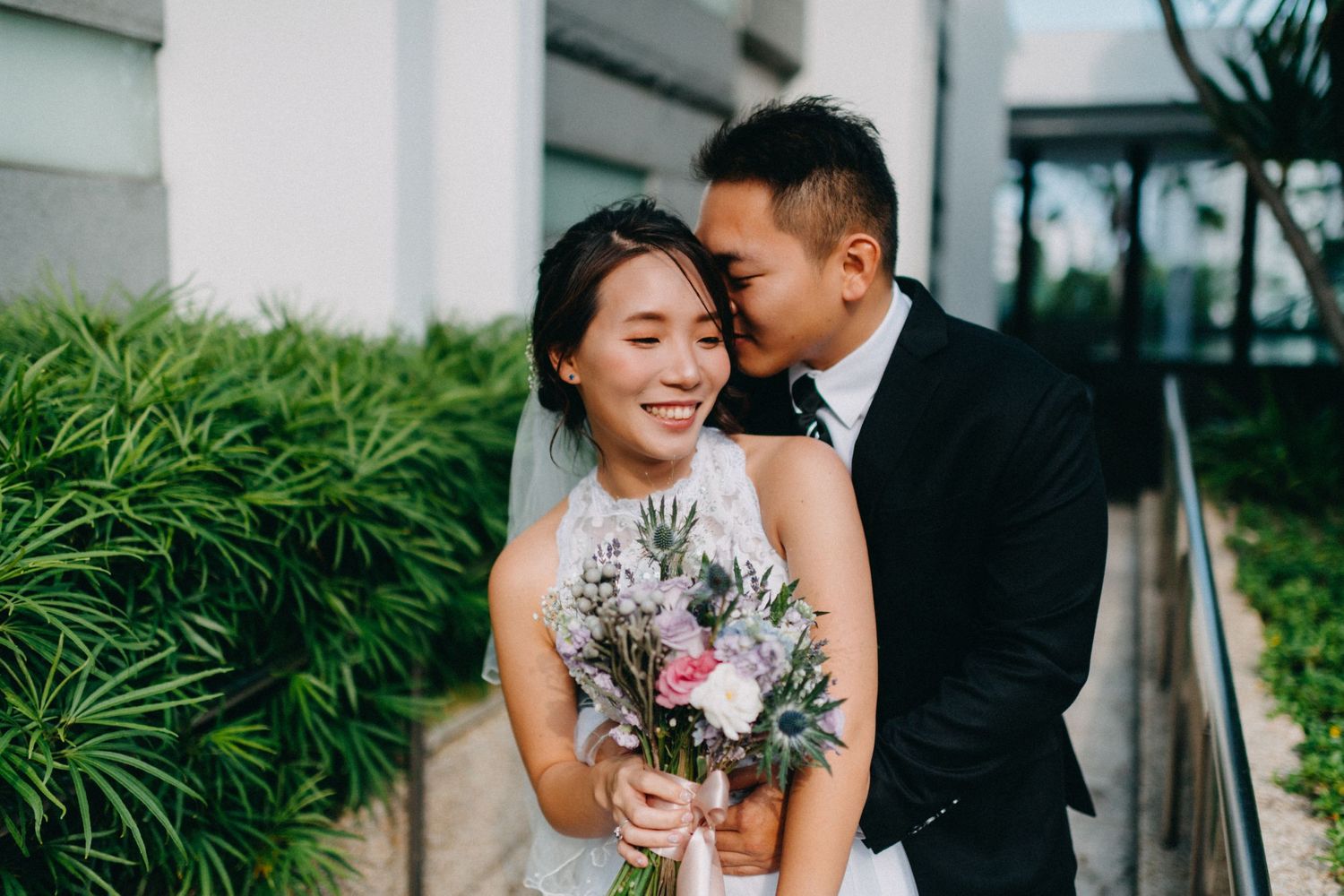 Wedding couple posing for portraits in a lush garden setting with greenery.