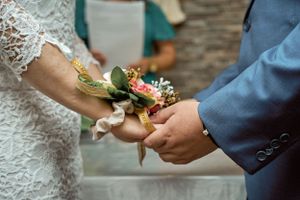 Close-up of hands exchanging a delicate corsage with pink flowers and greenery.