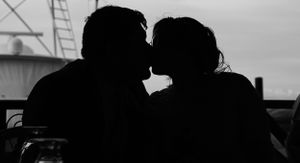 Silhouetted couple sharing an intimate moment against cloudy sky.