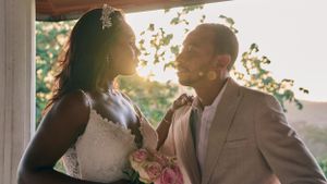 Romantic sunset wedding portrait with couple in elegant attire holding bouquet against golden light.