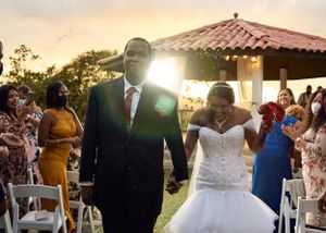 A joyful wedding ceremony at sunset with guests celebrating as newlyweds walk down the aisle under golden light.