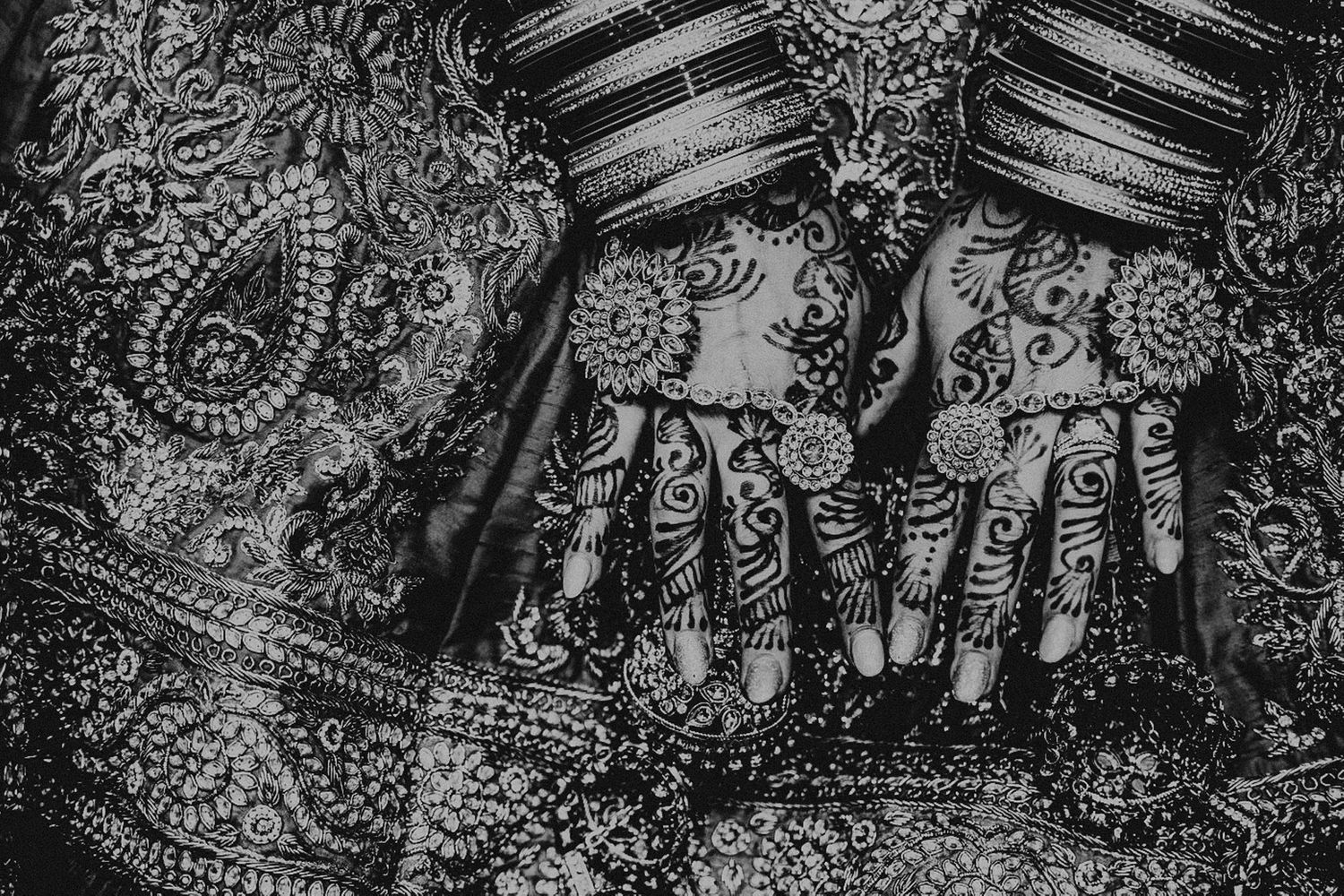 Close-up black and white photo of intricate henna designs on hands with traditional fabric.