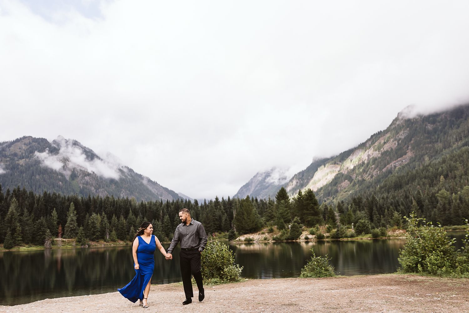 A couple dances by a mountain lake surrounded by evergreen forests and misty peaks.