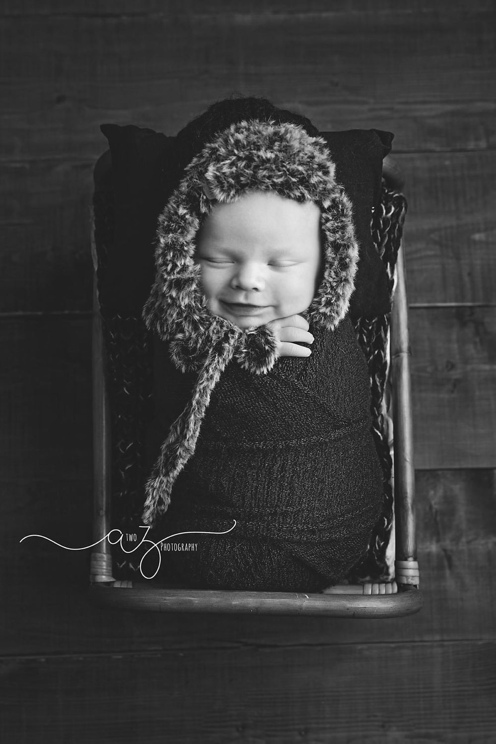 Sweet newborn napping in knit bonnet posed in vintage wooden chair.