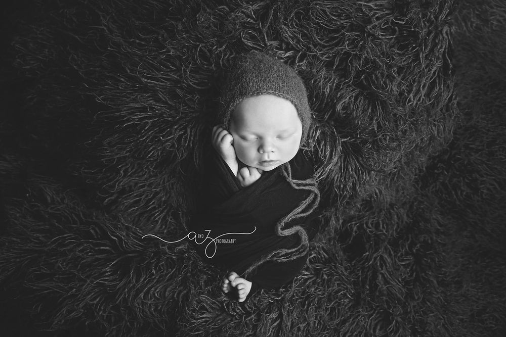 Peaceful newborn sleeping in black wrap on textured dark background.