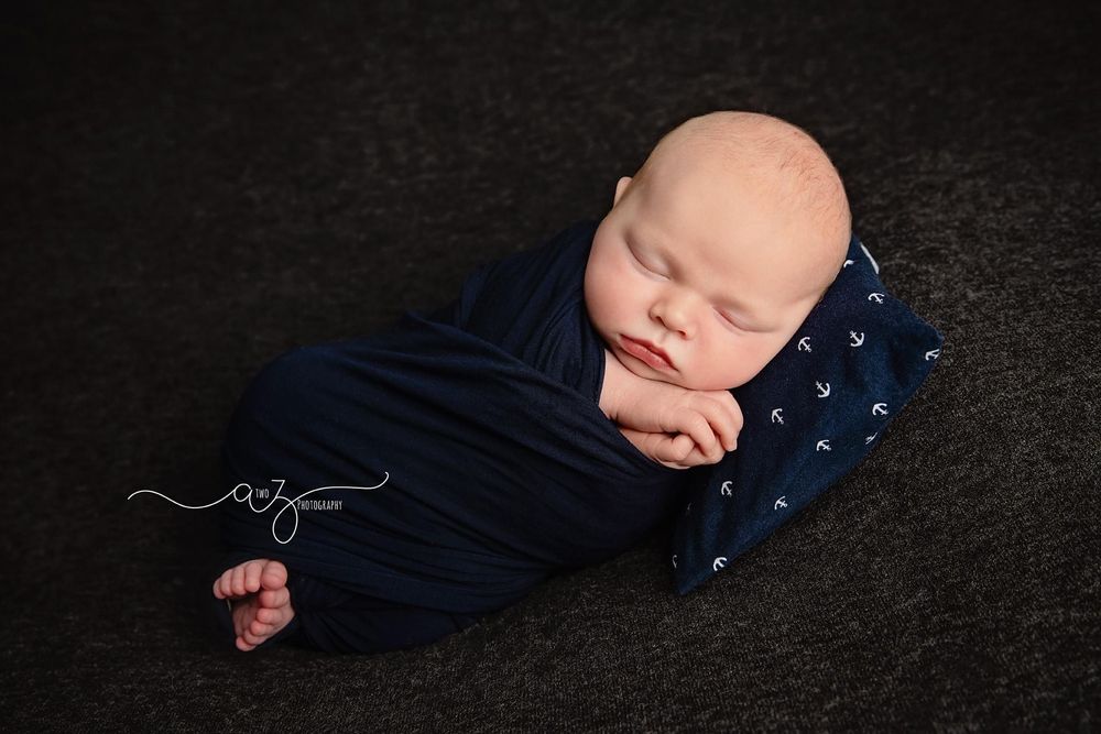 Sleeping newborn in navy outfit resting on starry pillow against black backdrop.