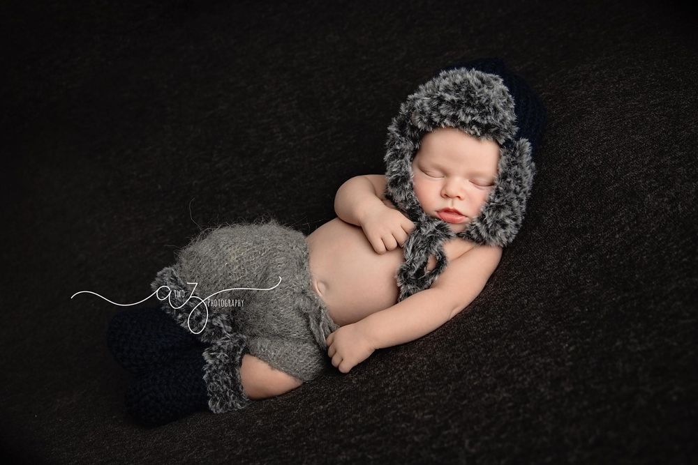 Newborn in cozy knit bonnet sleeps on dark background in professional portrait.