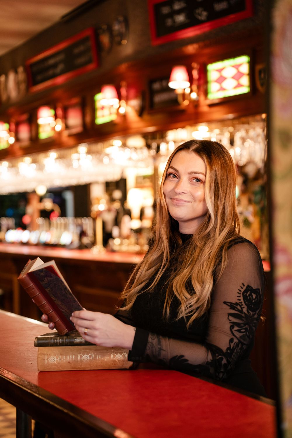 A customer reads a book at a vintage-style bar counter with stained glass lighting overhead.