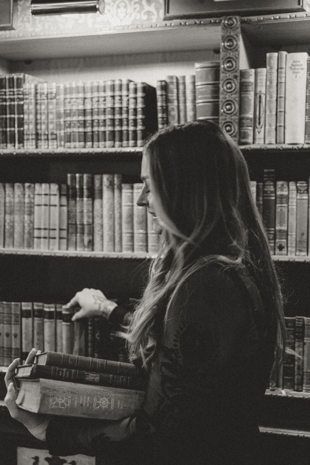 A silhouette browsing old books on wooden library shelves in black and white.