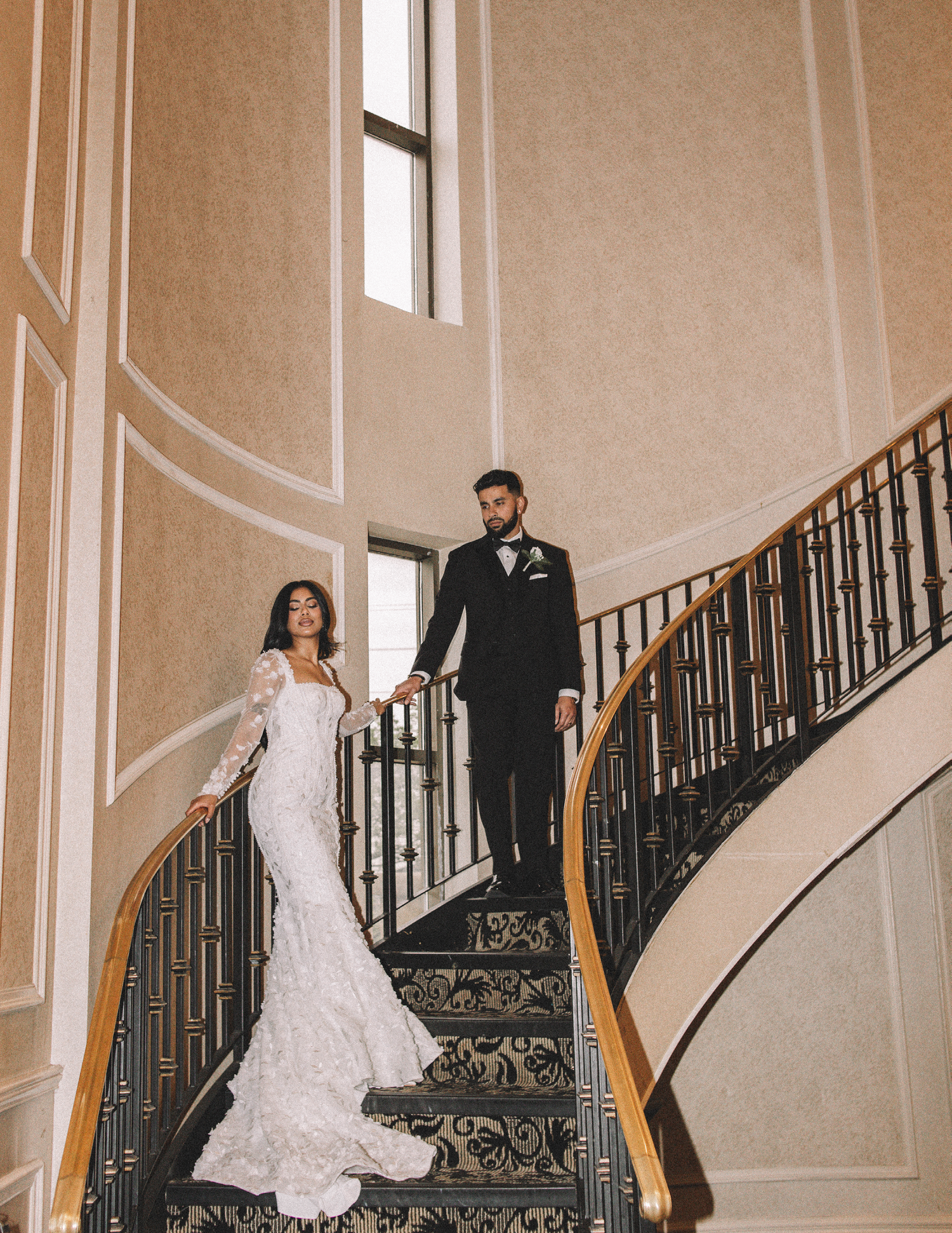 Elegant couple descending grand staircase in formal wedding attire.