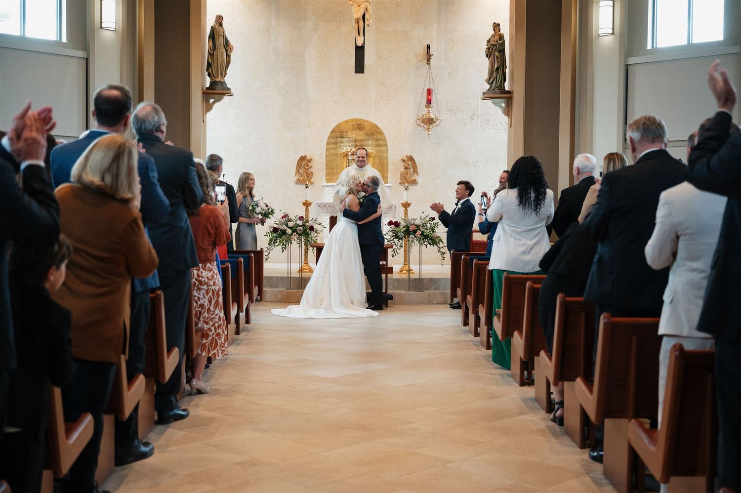 Wedding guests stand in church pews while watching a ceremony at the altar.