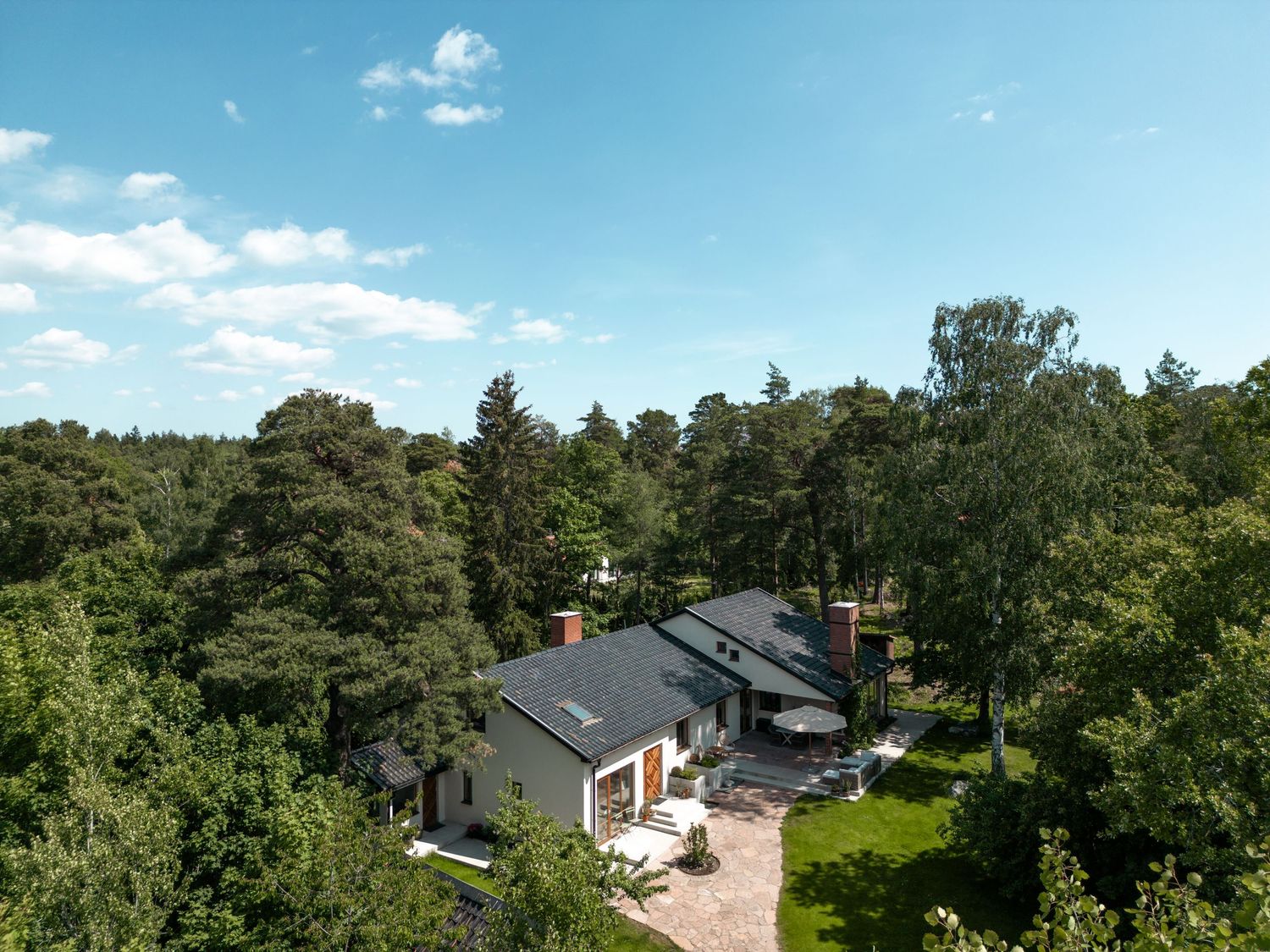 Aerial view of modern house with solar panels surrounded by green forest landscape on a sunny day.